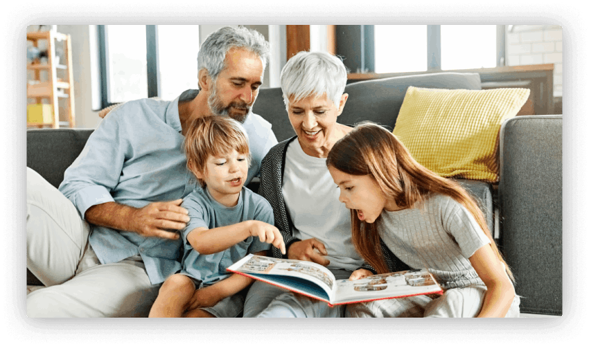 Grandparents and two young children sitting in a clean living room reading a picture book.