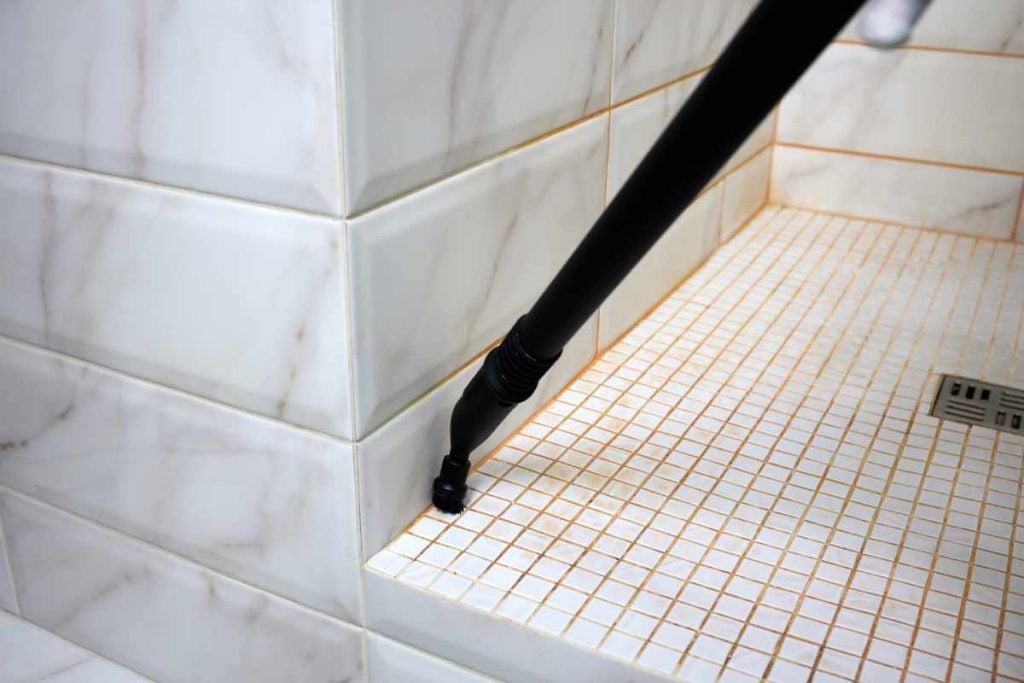 Professional cleaner using steam to clean the grout in a shower cabin