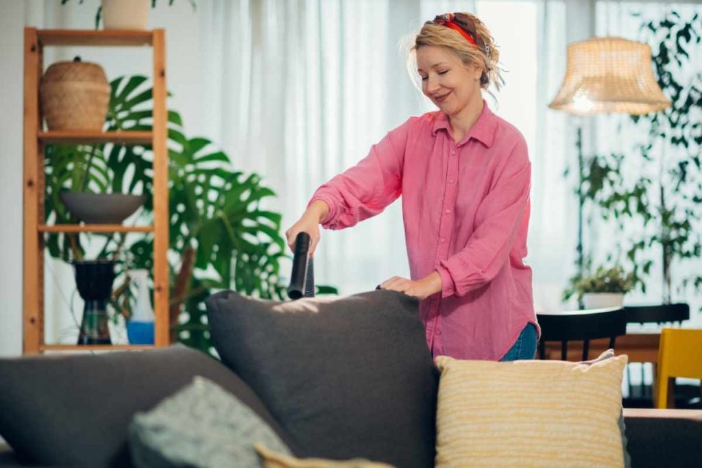 Woman using handheld vacuum cleaner to remove dust and mites from sofa