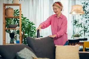 Woman using handheld vacuum cleaner to remove dust and mites from sofa