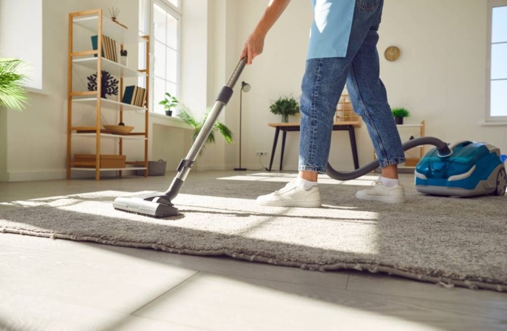 Woman cleaning carpet with vacuum cleaner in the living room at home.