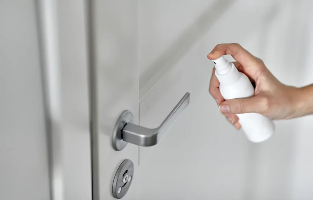 Hand spaying disinfectant or sanitizer to door handle surface