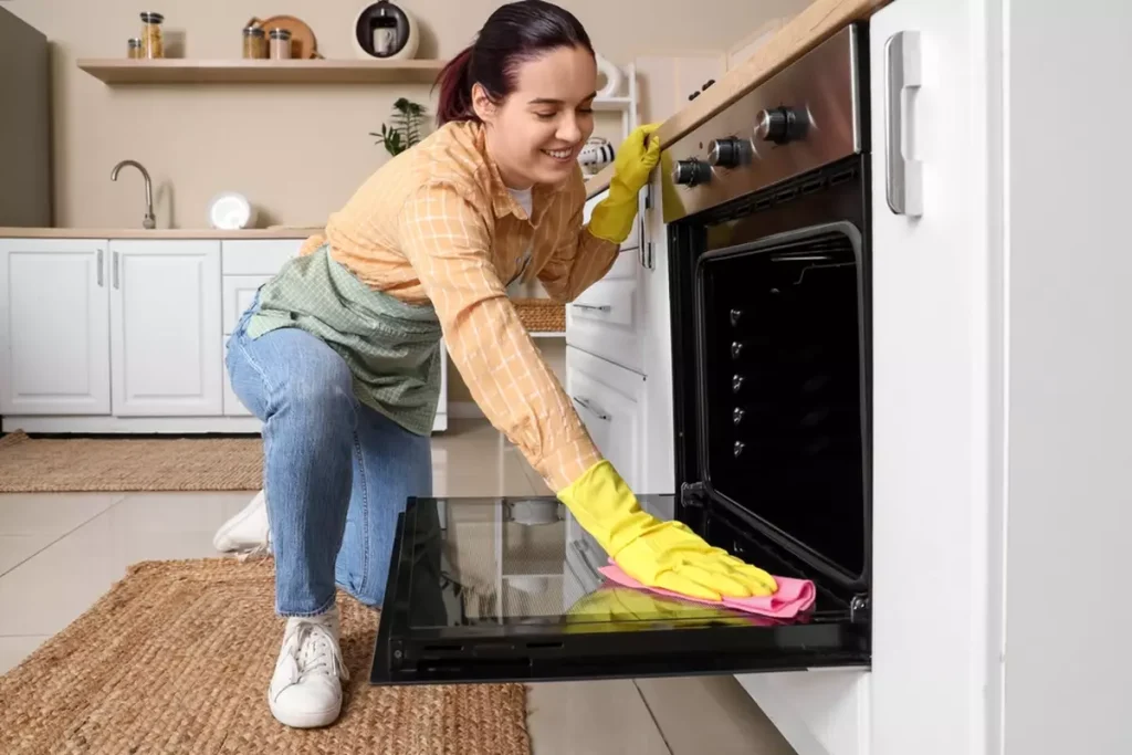 Young woman cleaning oven in kitchen