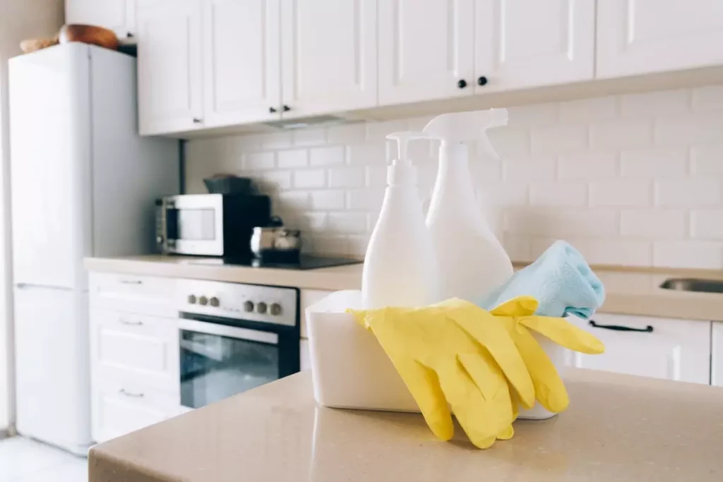 Cleaning supplies on kitchen counter with gloves and spray bottles.