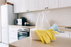 Cleaning supplies on kitchen counter with gloves and spray bottles.